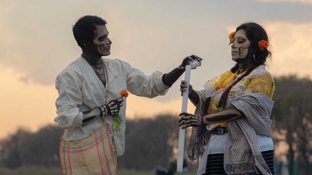 Celebrants in traditional Dia de los Muertos face paint and attire engaging in a cultural ritual outdoors.